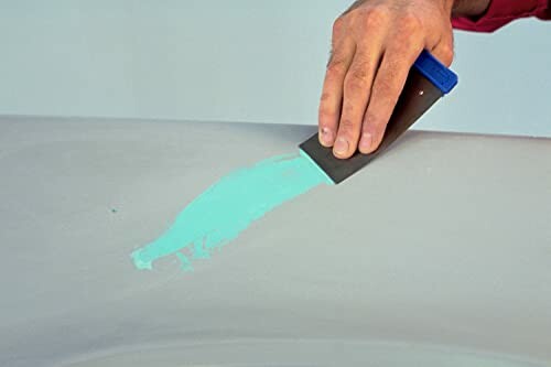 Hand applying green putty with a spatula on a surface.